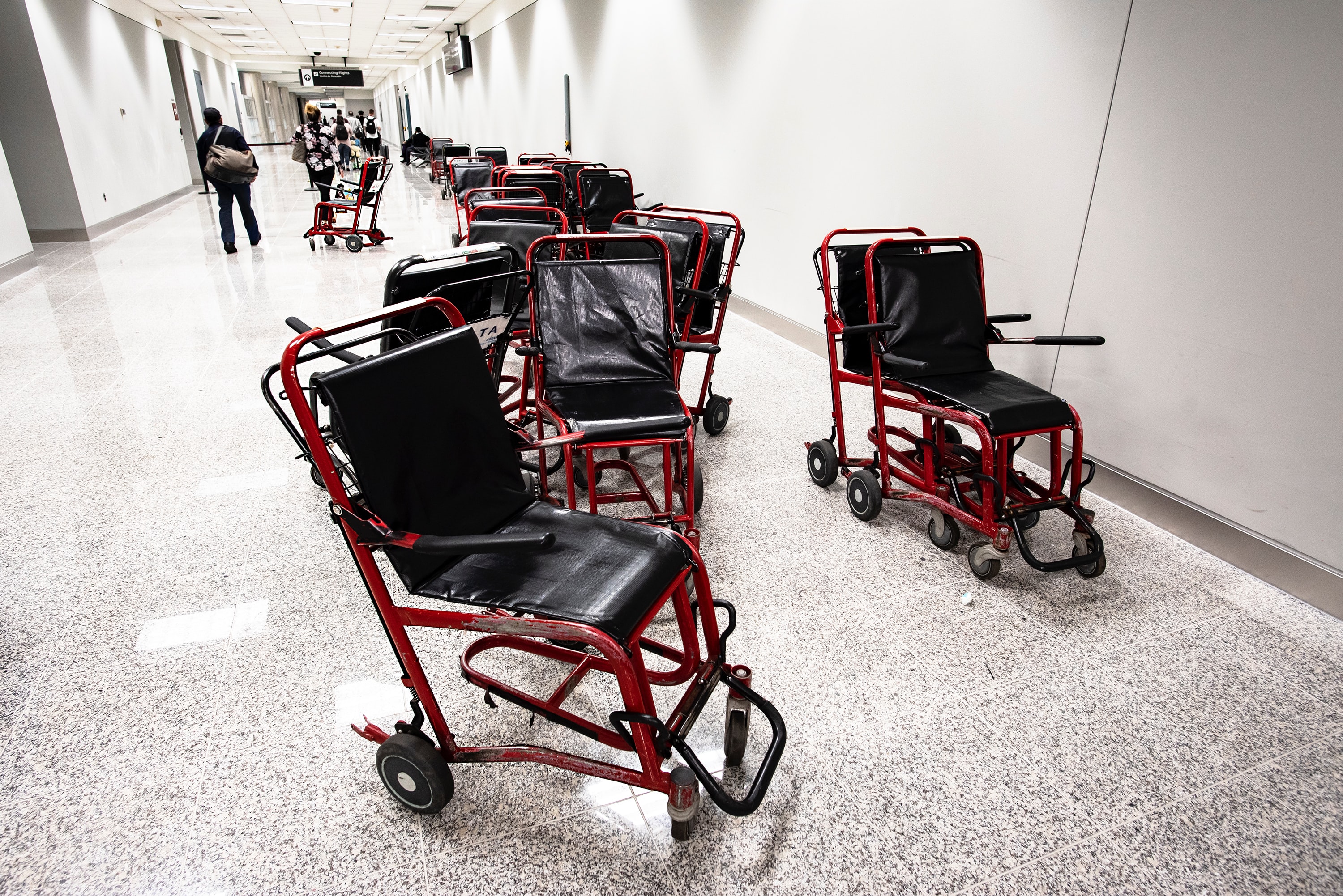 A cluster of worn-out transit wheelchairs stranded messily in an airport hallway.