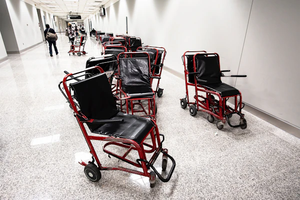 A cluster of worn-out transit wheelchairs stranded messily in an airport hallway.