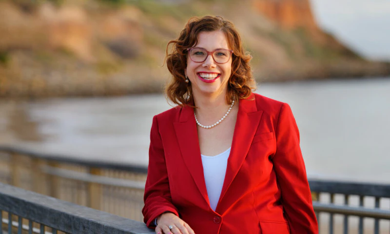 Labor Minister, Amanda Rishworth, is outside on a walkway near the water. She's smiling and wears a red blazer.