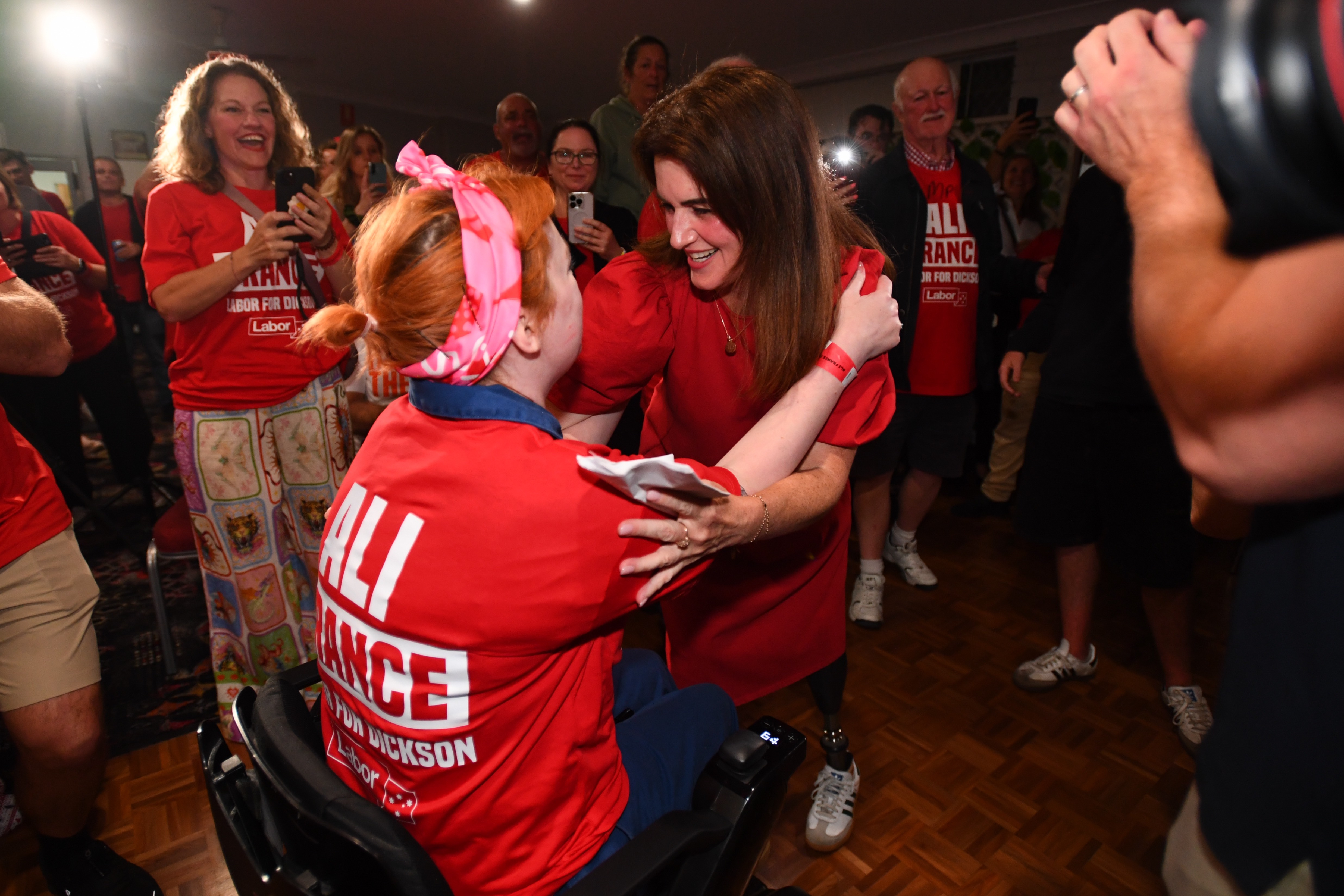 Disability advocate Elly Desmarchelier and Labor Party's Ali France embrace. They're at an election party and are wearing red coloured clothing.