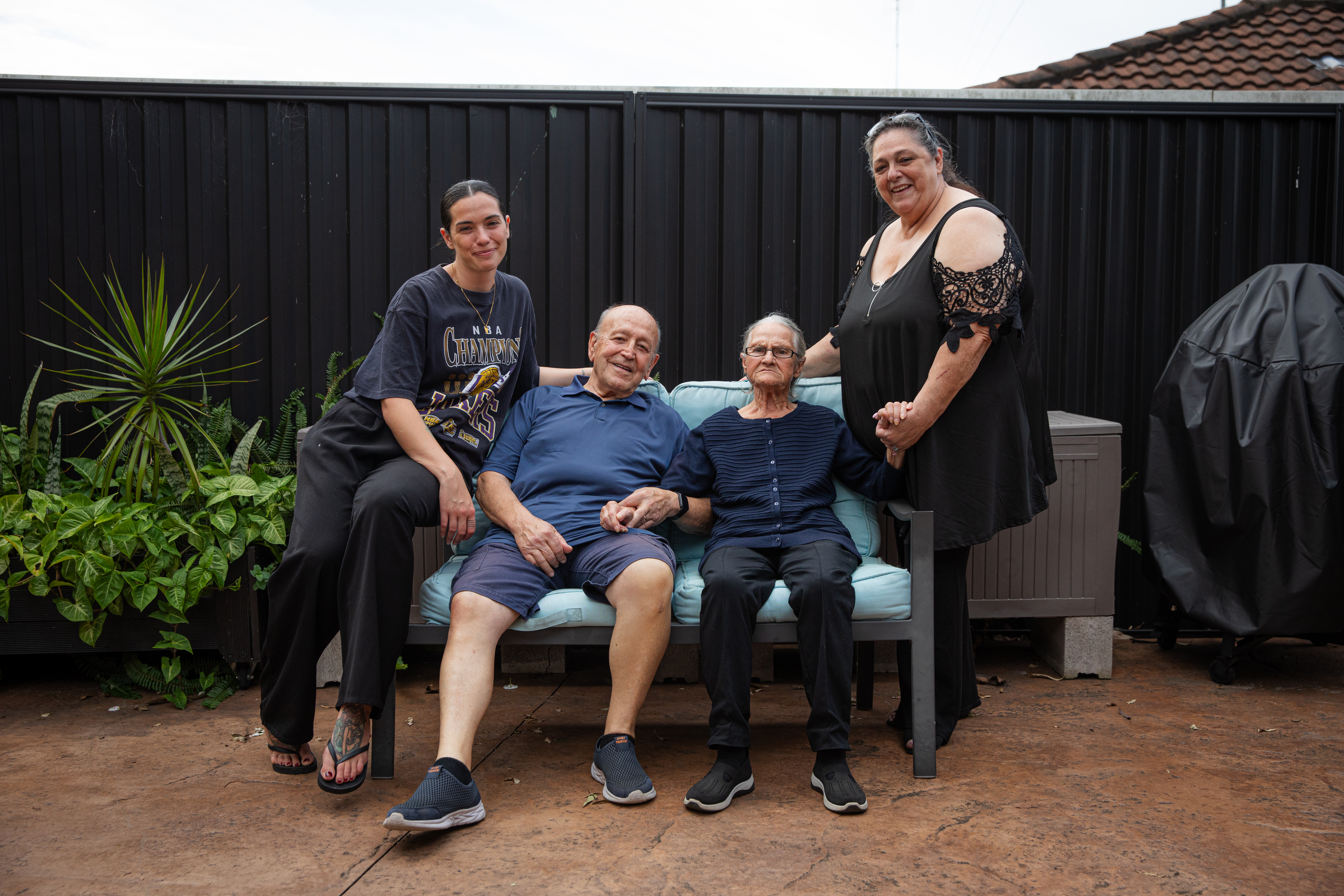 A Hireup aged care client, Victoria, is surrounded by her family. They are sitting outdoors.