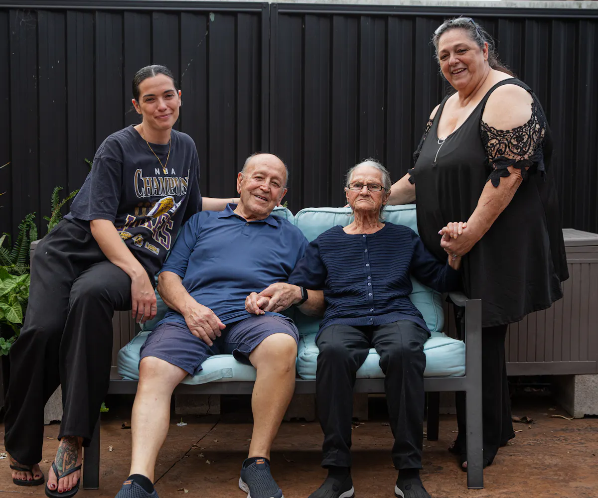 A Hireup aged care client, Victoria, is surrounded by her family. They are sitting outdoors.