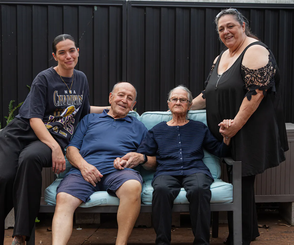 A Hireup aged care client, Victoria, is surrounded by her family. They are sitting outdoors.