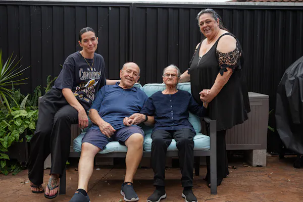 A Hireup aged care client, Victoria, is surrounded by her family. They are sitting outdoors.