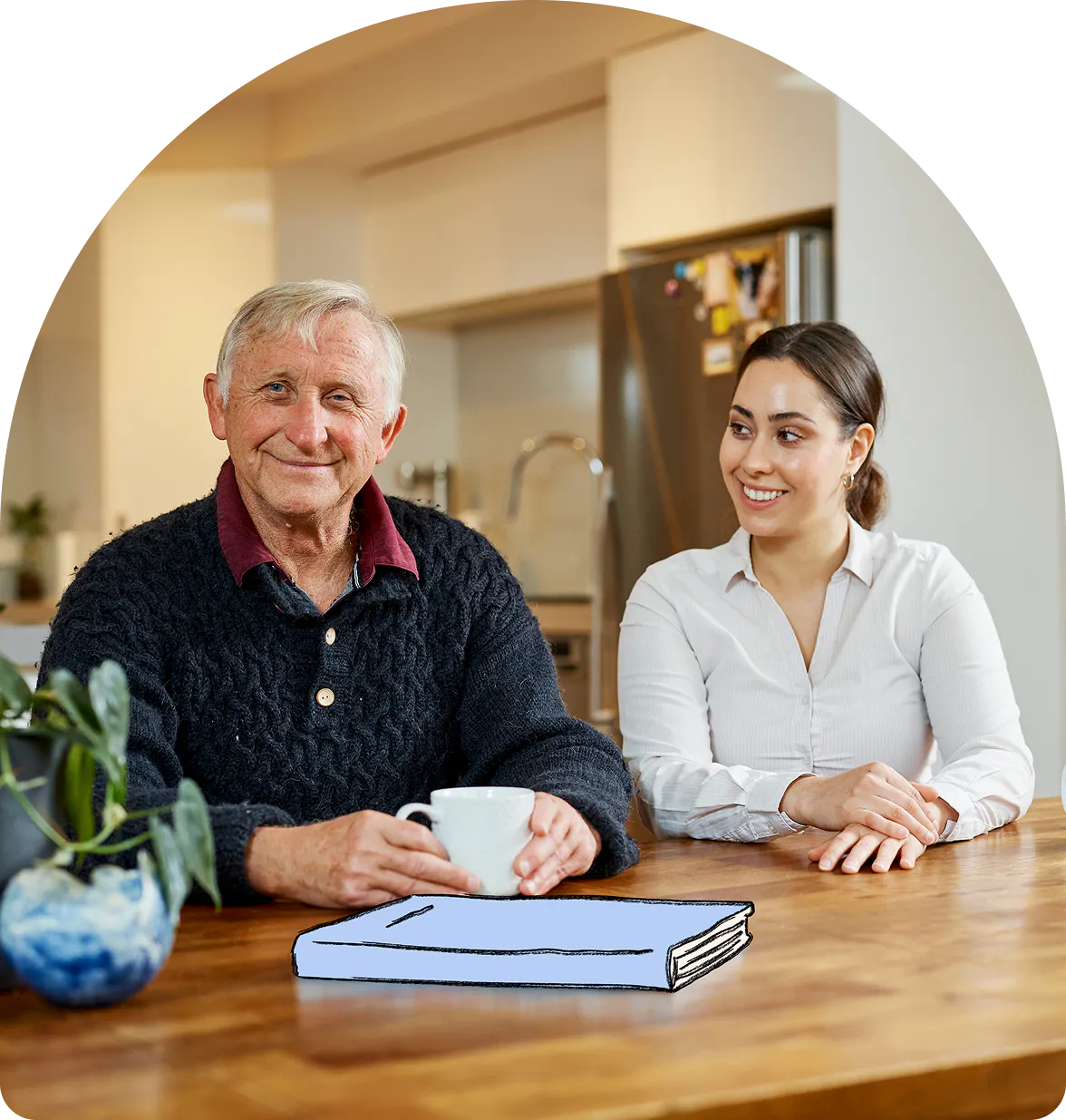 Hireup client Dirk and support worker Brenda smile over a cup of tea and a book.