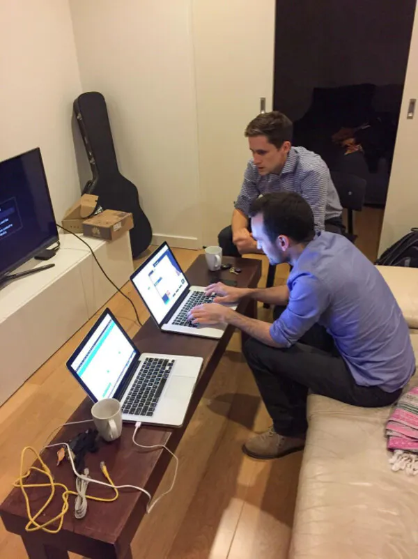 Jordan and Murray are sitting in a house with two open laptops in front of them. They are surrounded by cords and coffee mugs