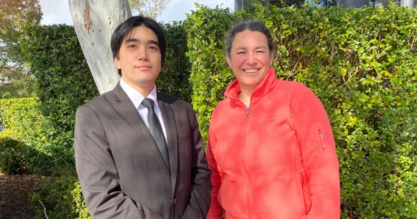 A photo of Chem and his Hireup teammate smiling at the camera. Chem wears a professional suit and tie with his hands placed in front of him. His team mate wears a pink jumper and has her hair tied back.