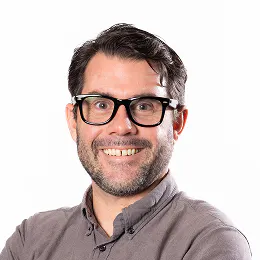 A smiling headshot of Dave Collins. He wears glasses and has short brown hair.