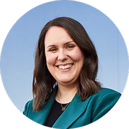 A smiling headshot of Laura O’Reilly. She wears a green jacket and has brown, shoulder length hair.