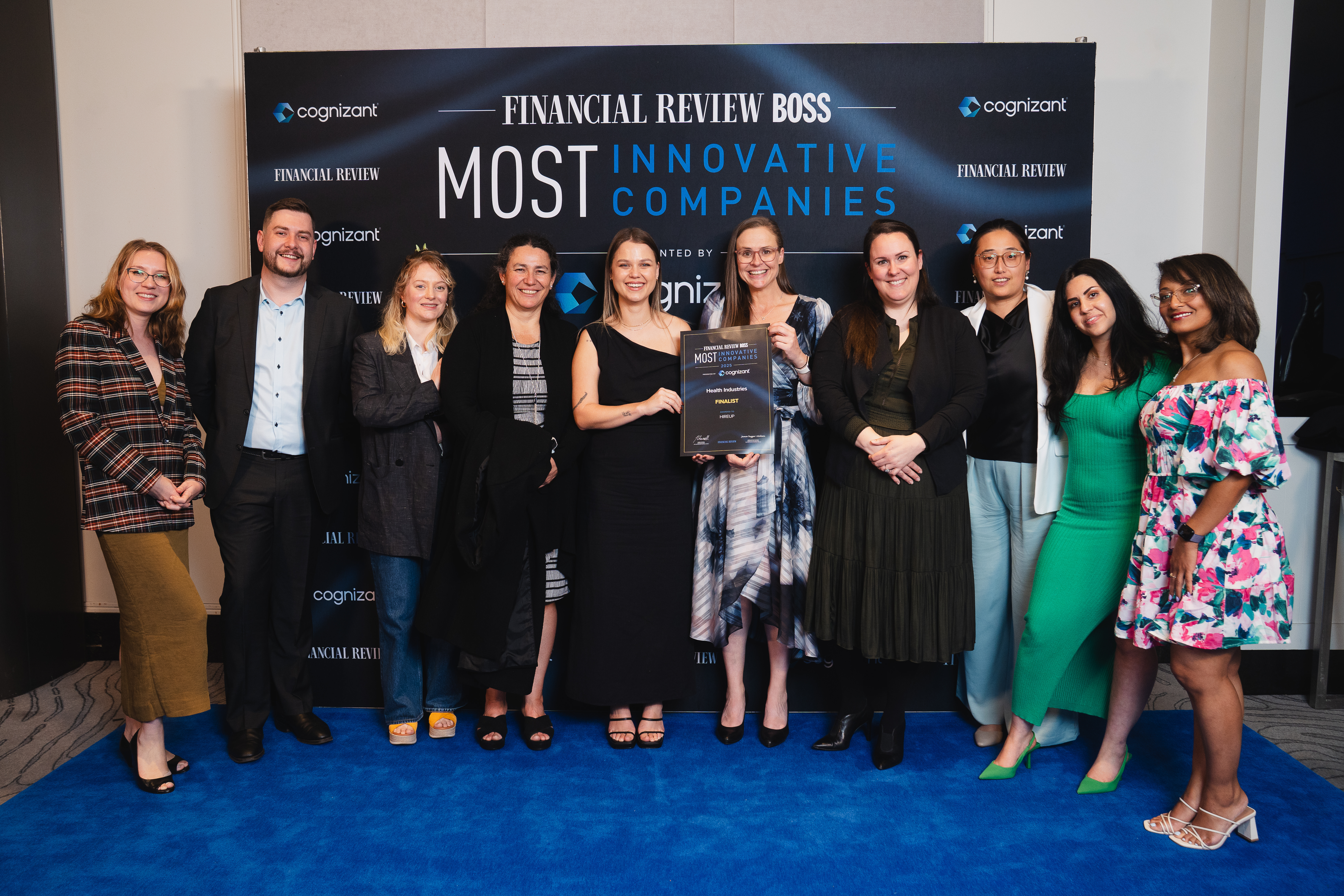 A group of ten Hireup team members are at the Australian Financial Review Boss Awards night. They're gathered in front of a media wall that has  the AFR logo, and two of them are holding a large certificate.