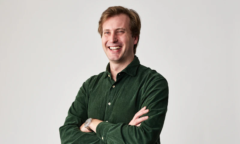 Peter Willis, Hireup's CEO, has short, brown hair and is wearing a dark, green corduroy shirt. He's smiling, with his arms folded, in front of a white wall.