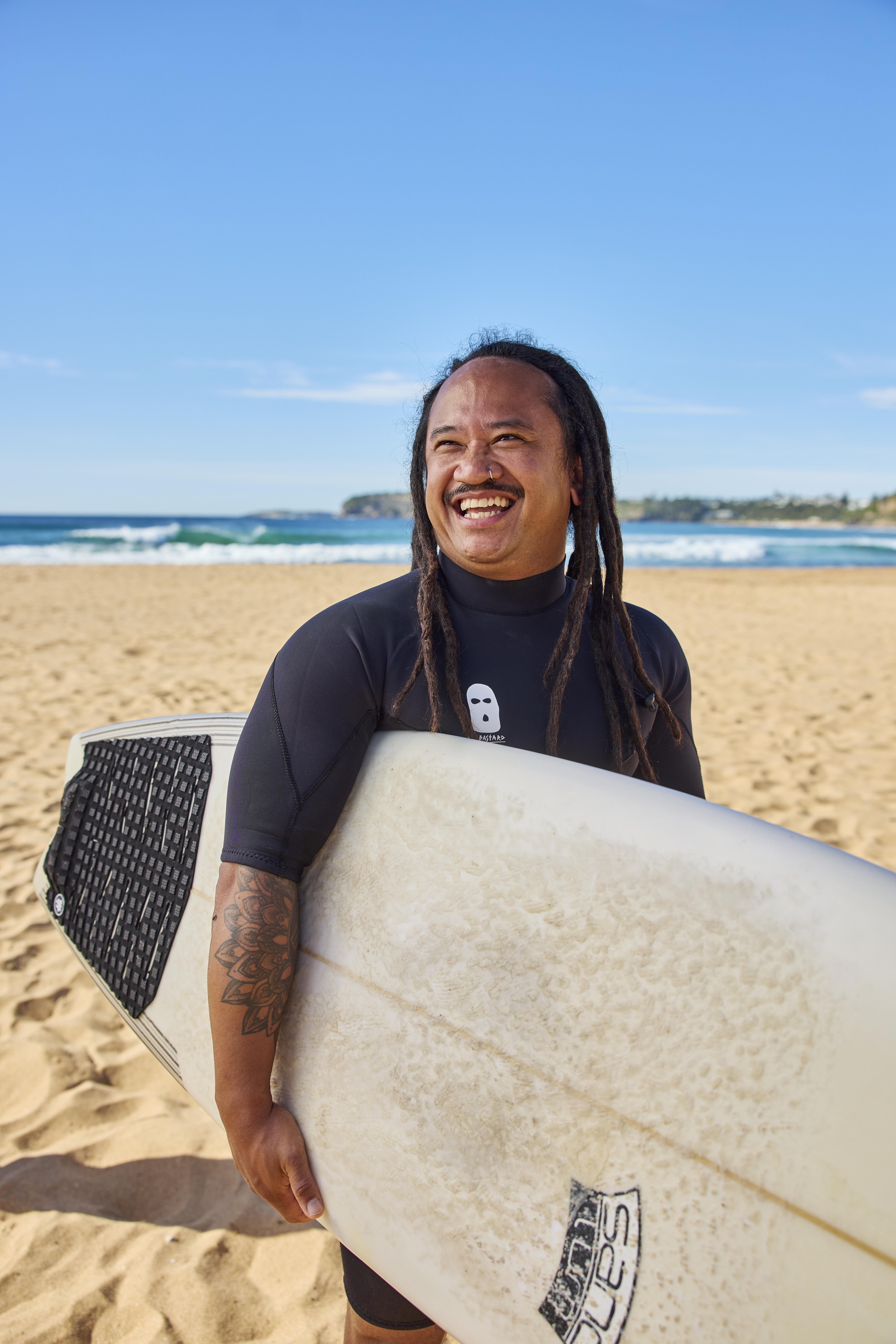 Hireup support worker Joey Pangilinan holding his surfboard on the beach.