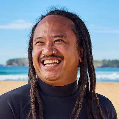 Hireup support worker Joey Pangilinan holding his surfboard on the beach.