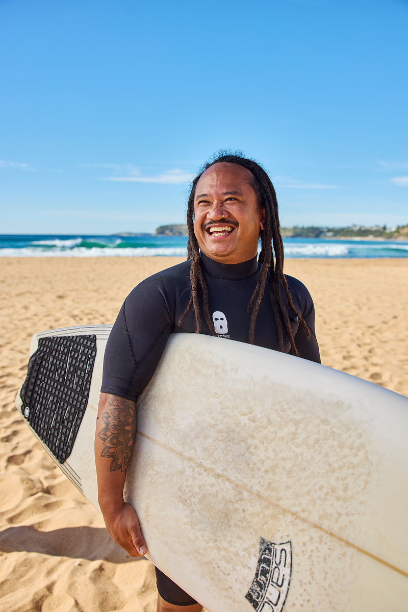Hireup support worker Joey Pangilinan holding his surfboard on the beach.