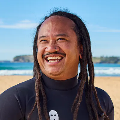 Hireup support worker Joey Pangilinan holding his surfboard on the beach.