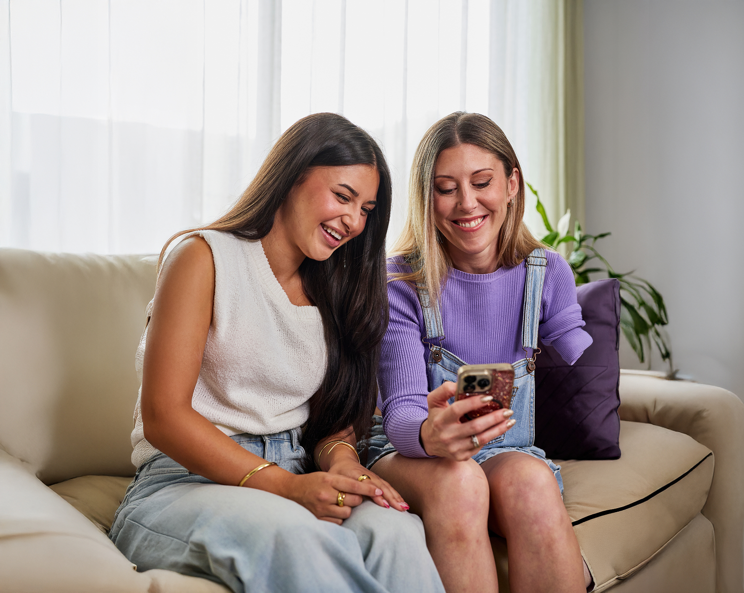 Hireup client Deb shows her support worker Allyah her phone. They're laughing together on the couch.