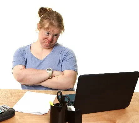 A woman frowning in front of a computer with her arms crossed.
