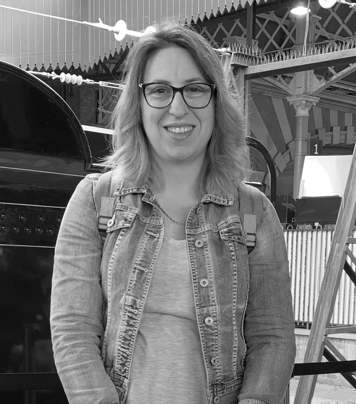 Melissa Ward has long blonde hair and wears glasses and a denim jacket. She smiles at the camera. 