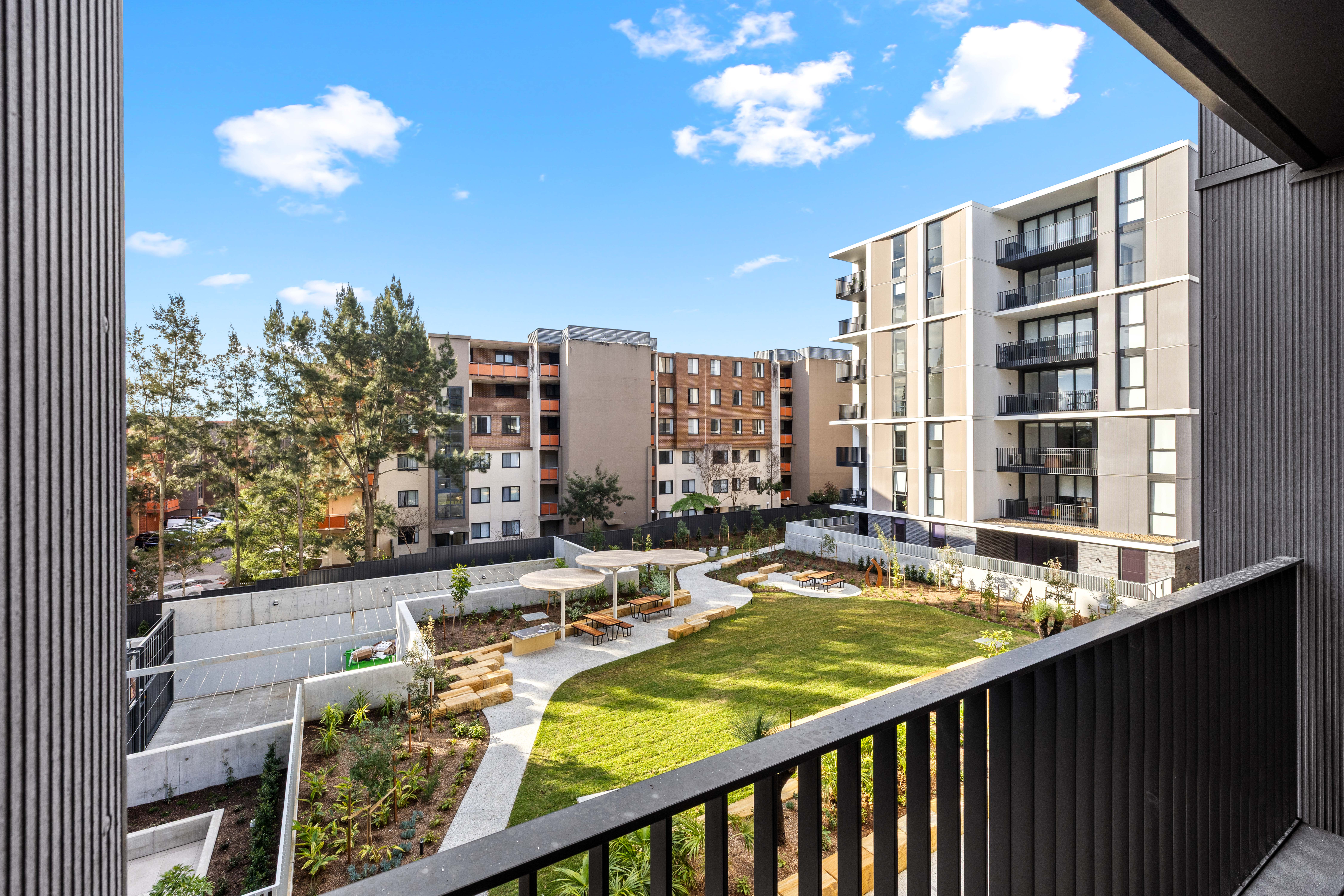 The view from the balcony of an MyLife Community Housing apartment. It looks over another wing of the apartment complex, plus a communal garden and sitting area.  