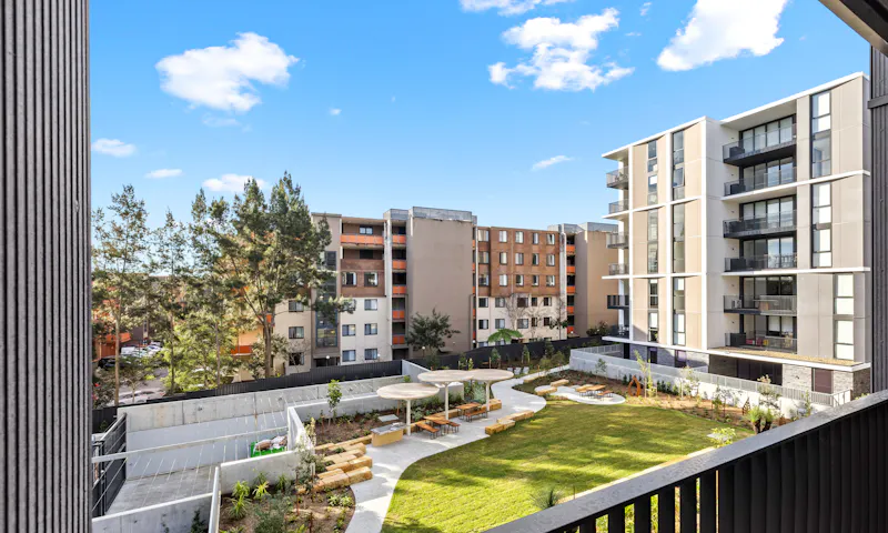 The view from the balcony of an MyLife Community Housing apartment. It looks over another wing of the apartment complex, plus a communal garden and sitting area.