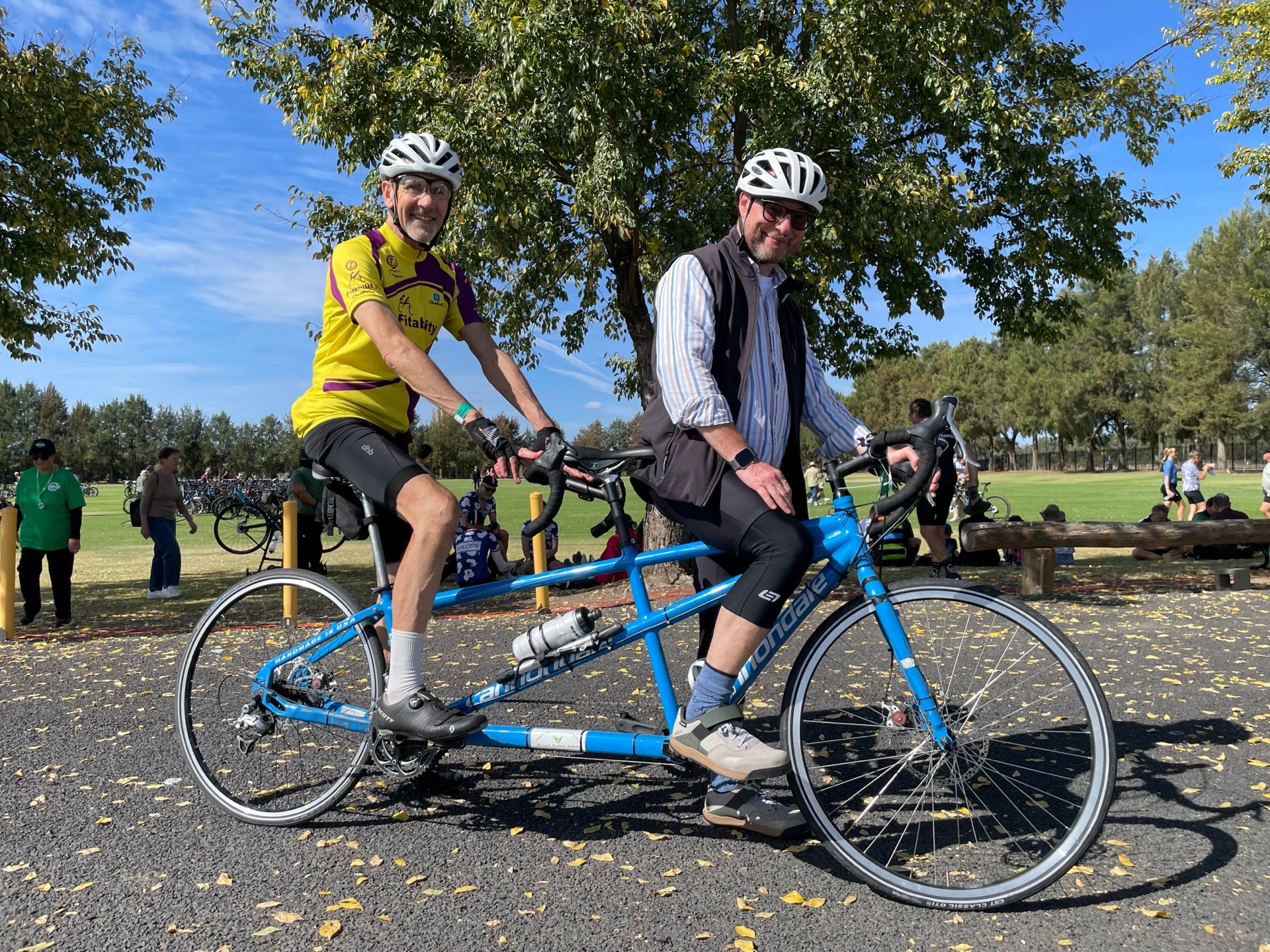 Andrew and his tandem partner, Leo, are at a park. They're wearing helmets, riding gear and are sitting on a blue tandem bike.
