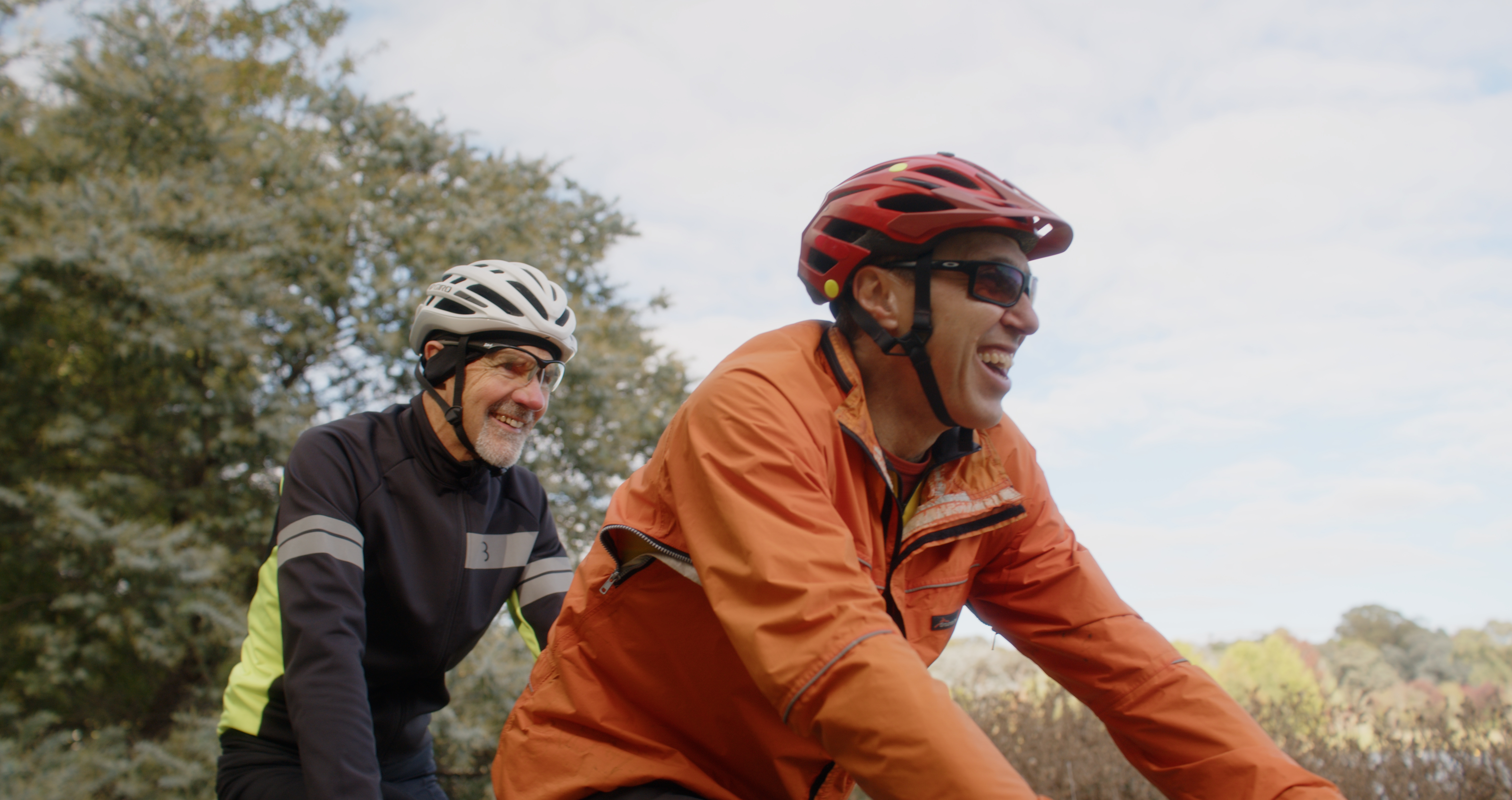 Andrew is riding a tandem bike with his Hireup support worker. They're both wearing helmets and jackets.