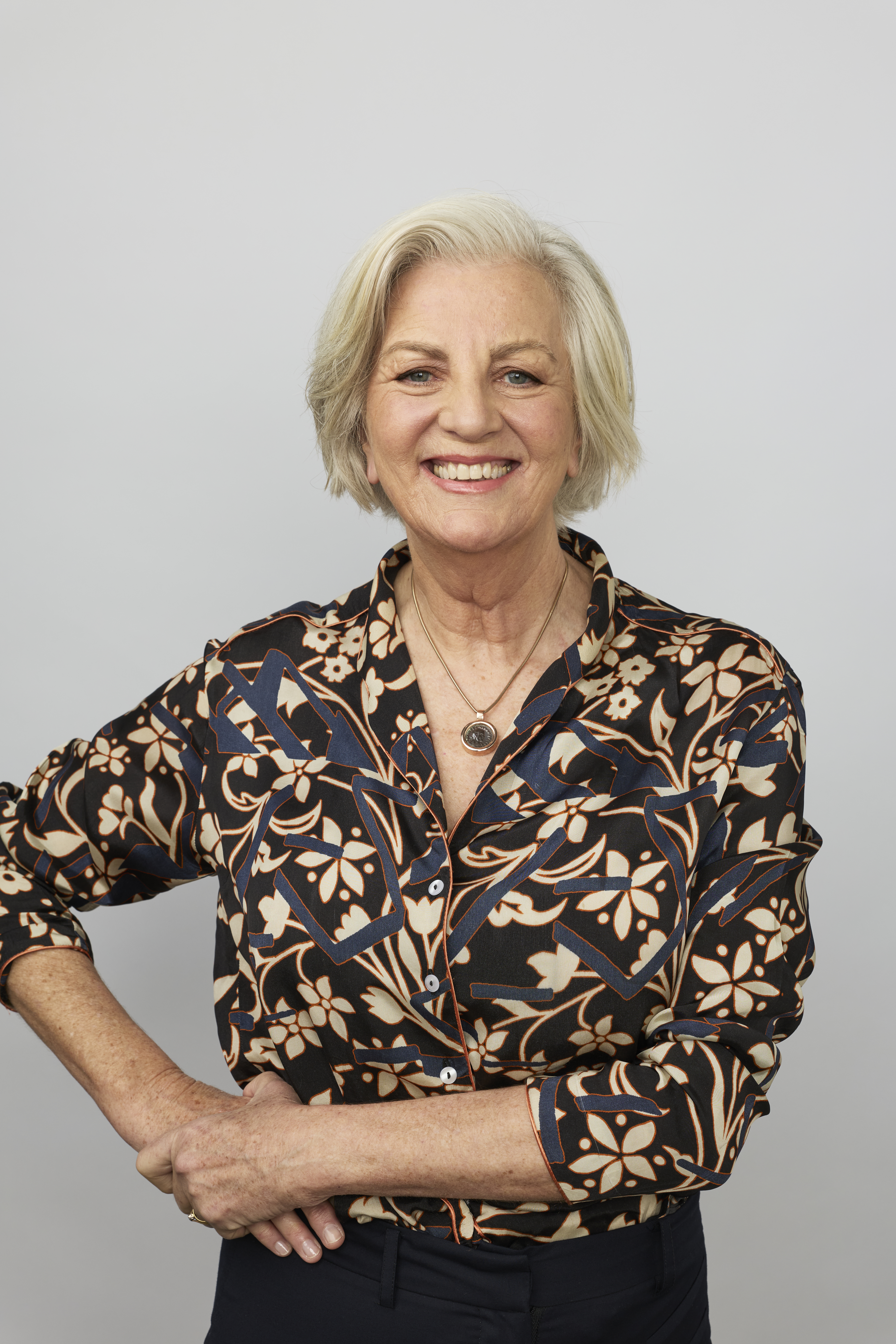 Jean Kittson stands in front of a studio wall. She rests a hand on her hip and wears a navy top with a floral pattern.