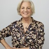 Jean Kittson stands in front of a studio wall. She rests a hand on her hip and wears a navy top with a floral pattern.