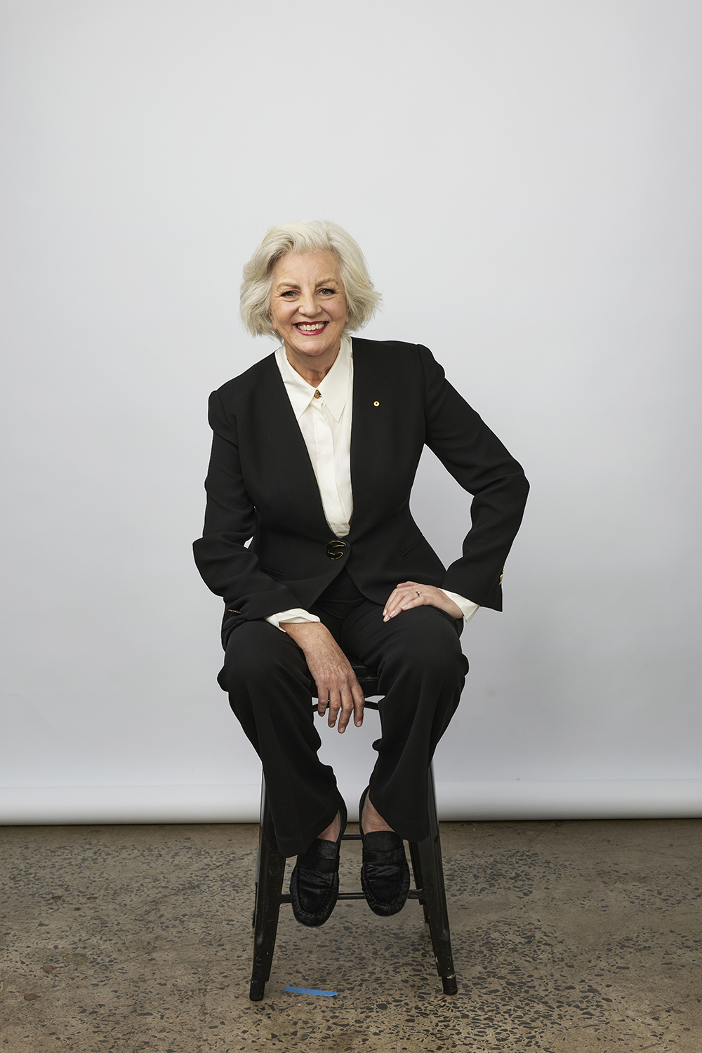 Jean Kittson is sitting on a stool. She has light grey hair and is wearing a black pant suit.&nbsp;