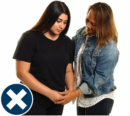 A woman supporting another woman, holding her hand. There is a cross next to them