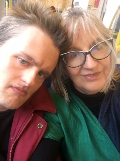 Thea and her son Julian are smiling together taking a selfie. They are on a train.