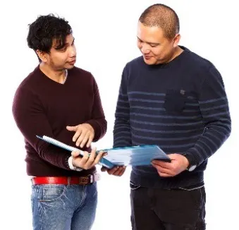 Two men look at a folder together. One man is talking and the other man is listening.