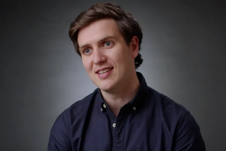 Hireup CEO Jordan O'Reilly is talking to the camera in front of a dark grey background. He wears a navy collared shirt.