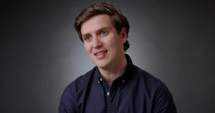 Hireup CEO Jordan O'Reilly is talking to the camera in front of a dark grey background. He wears a navy collared shirt.