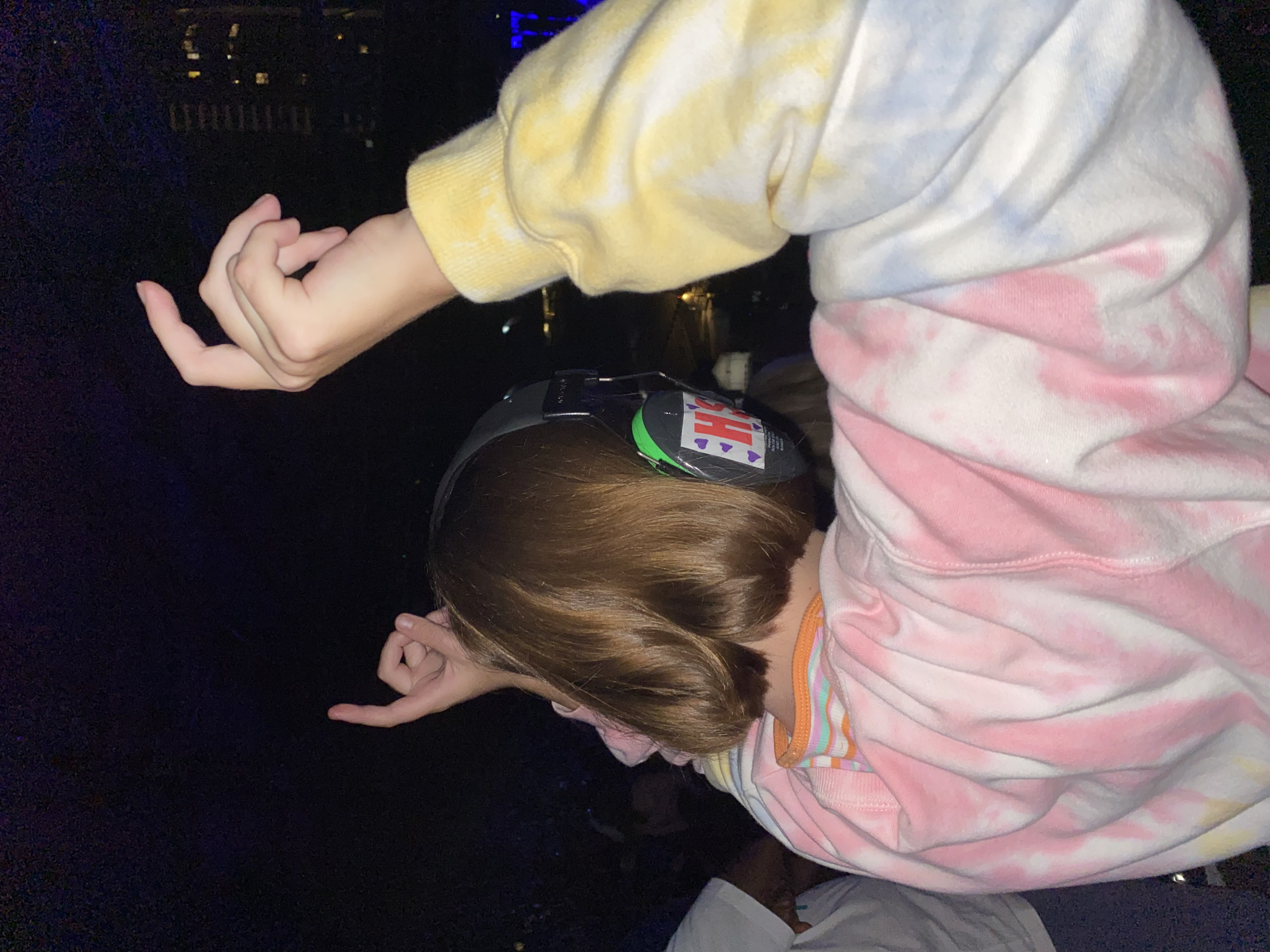 A teenager wearing noise-cancelling headphones and a colourful jumper rocks out at a music concert.