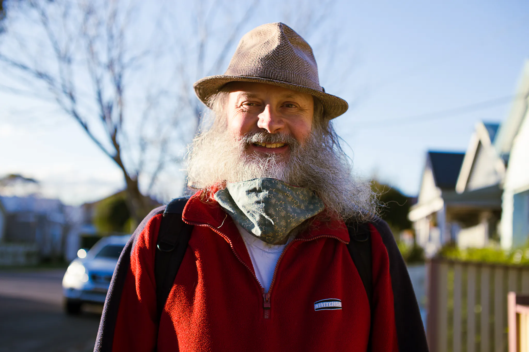 Andrew, a man with a big, bushy grey beard is smiling. He is wearing a hat with a brim.