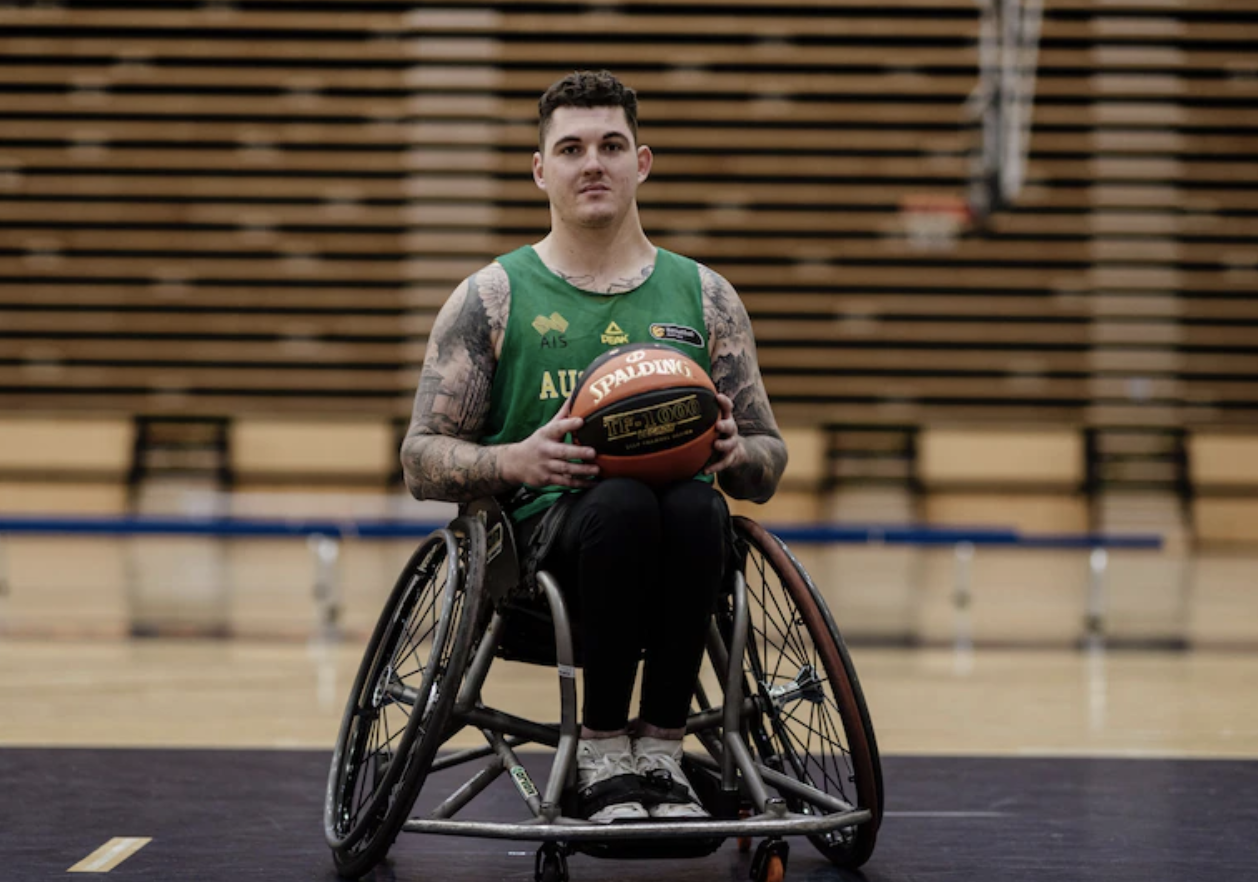 Australian wheelchair basketball player Jeremy Tyndall is on a basketball court. He's holding a basketball and looking at the camera. 