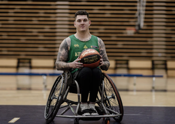 Australian wheelchair basketball player Jeremy Tyndall is on a basketball court. He's holding a basketball and looking at the camera.