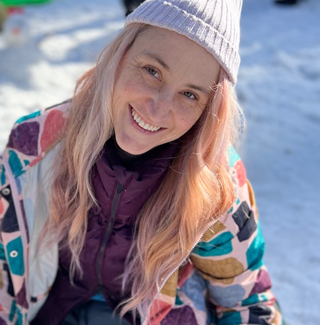Disability advocate Holly Karten has long blonde hair and wears a pink beanie and colourful jacket. She smiles at the camera. 