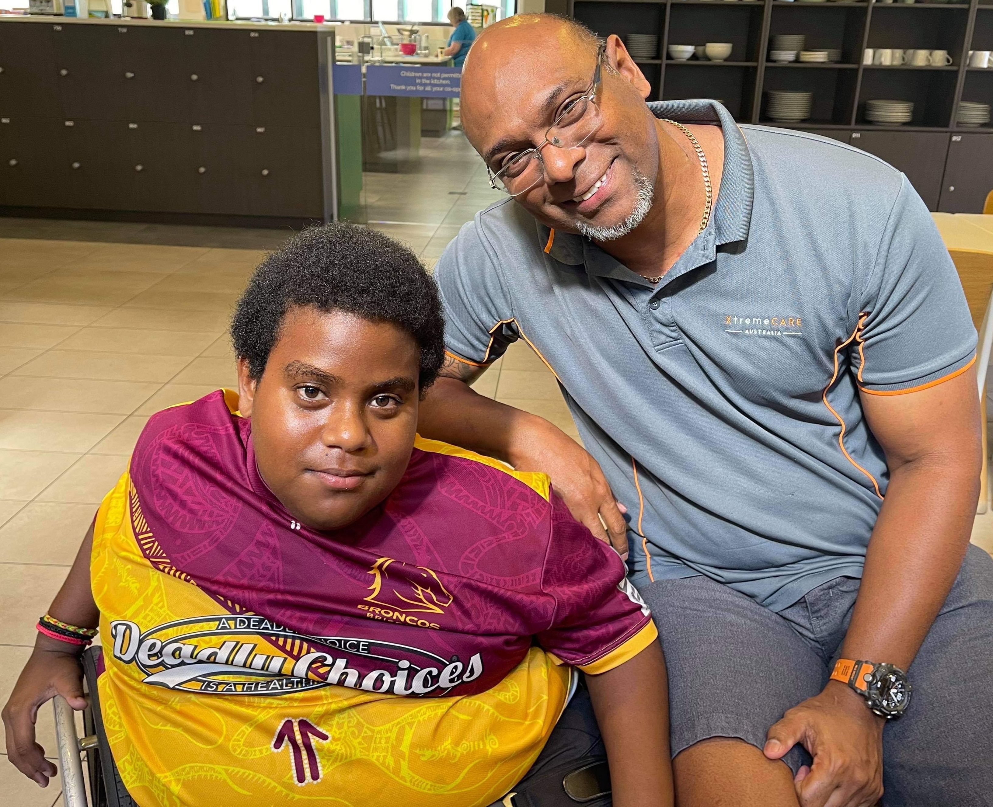 William Tatipata, co-founder and owner of XtremeCARE Australia, sits with Charlie Kris, an NDIS participant, on Thursday Island, Torres Strait.