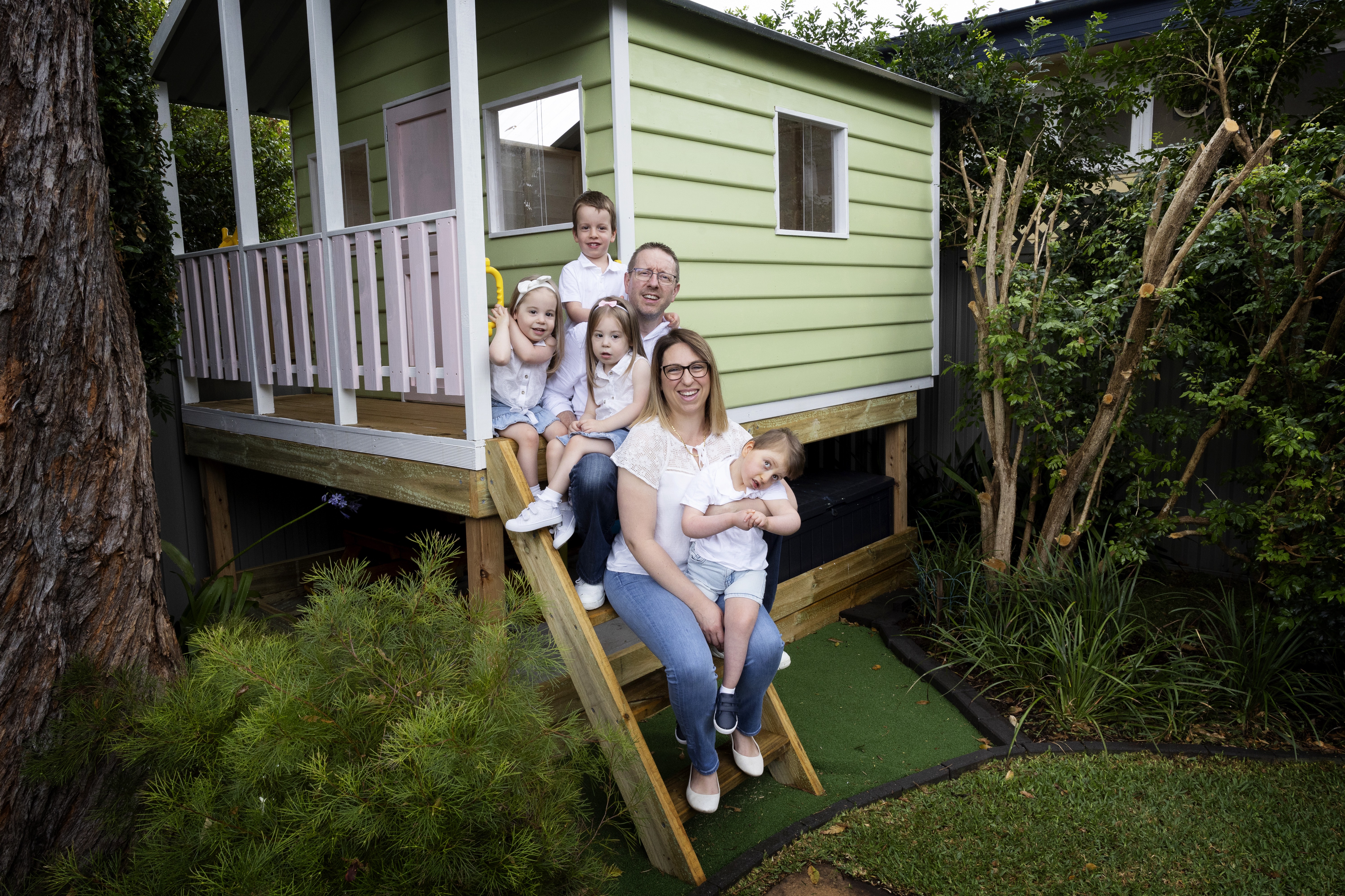 A family of four - including two sets of twins - sit on the steps of their backyard tree house. 