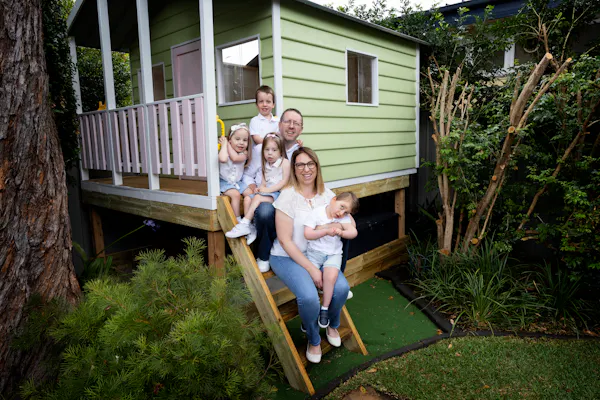 A family of four - including two sets of twins - sit on the steps of their backyard tree house.