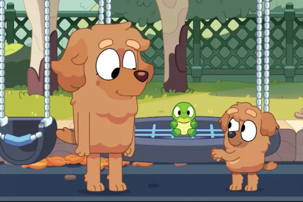 A still from an episode of Bluey, 'Turtleboy', featuring a non-speaking puppy with their mum on a playground, playing with a turtle toy on a swing.