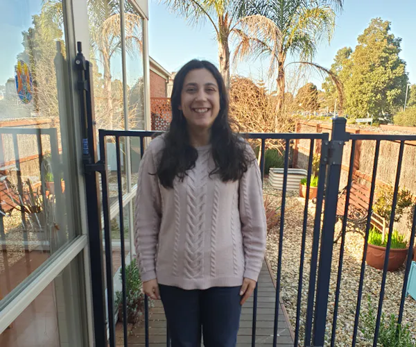 Disability activist and writer Laura Pettenuzzo stands smiling on a deck in garden on a sunny day.