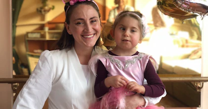 Holly is wearing a unicorn headband and is smiling. Her arm is wrapped around her daughter who's wearing a pink tutu.