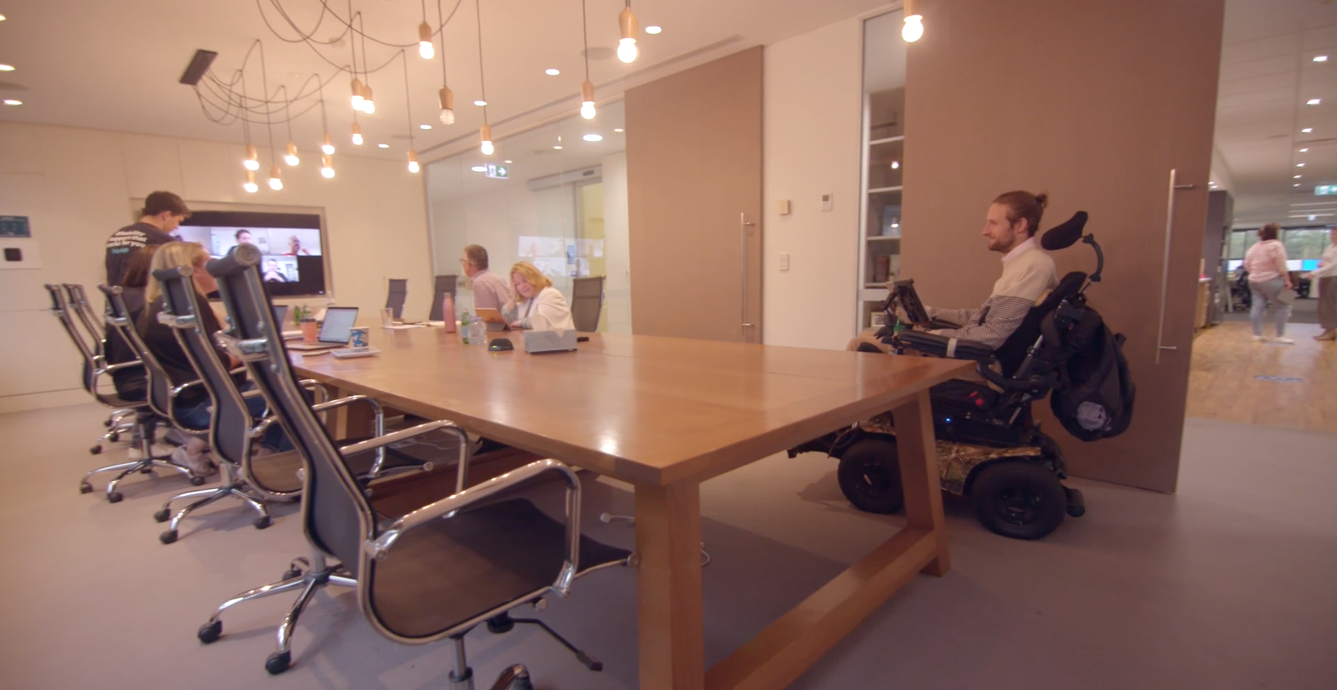 The Hireup board gathering in a board room. Steve is coming through the door. Steve is using a wheelchair.