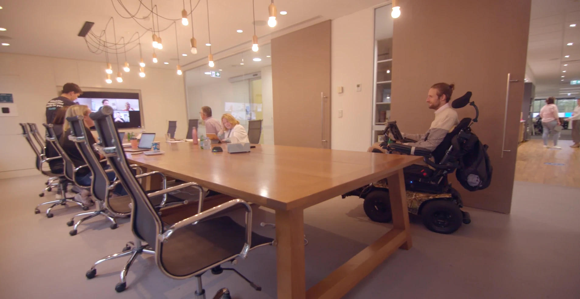 The Hireup board gathering in a board room. Steve is coming through the door. Steve is using a wheelchair.