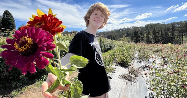 Image of author's son smiling and holding a bouquet of flowers toward the camera. It's a beautiful sunny day.