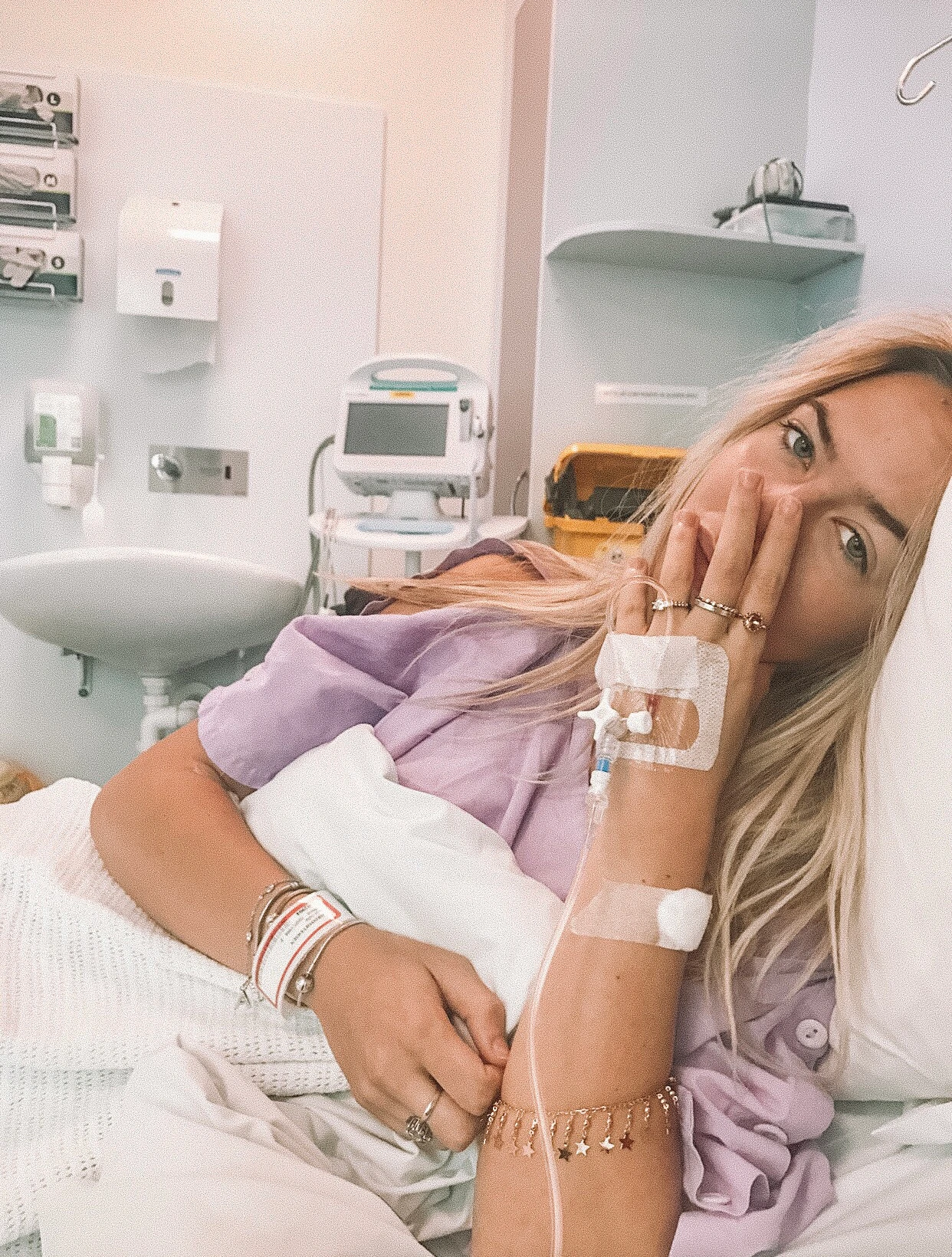 Anja is lying on her side in a hospital bed with her hand covering her mouth.
