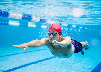 A young man is swimming in a lap pool. He wears a red cap and goggles.